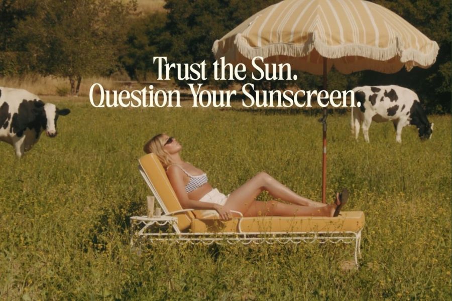 Trust the sun. Question your sunscreen campaign photo, woman lying on chaise lounge with cows in the backdrop
